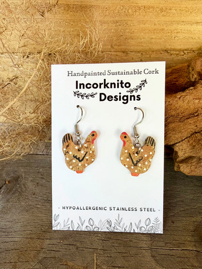 Handpainted natural cork chicken earrings on silver hooks, displayed on Incorknito Designs branded card with dried grass and cork bark background