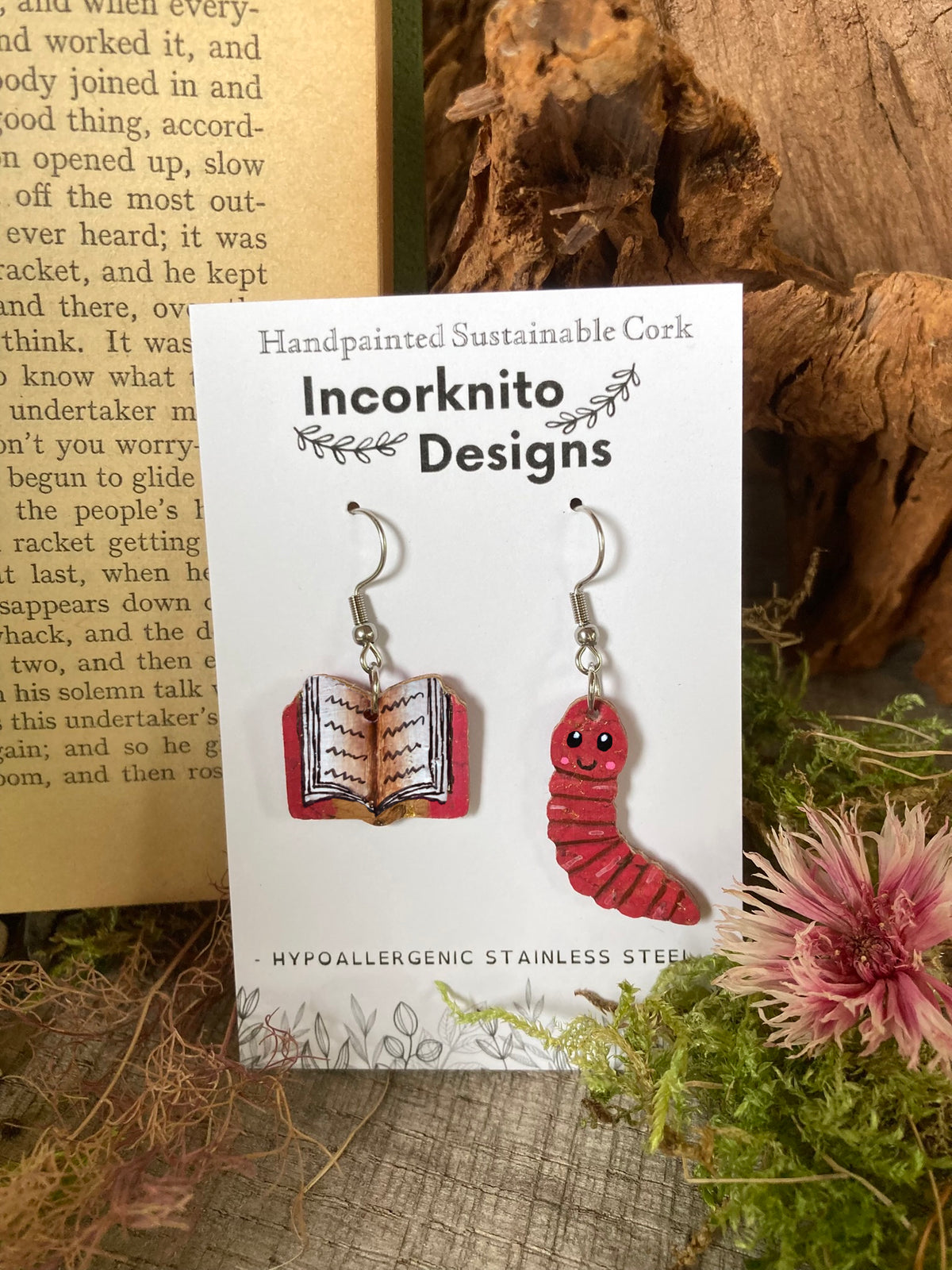 Handpainted cork bookworm earrings on silver hooks displayed on Incorknito Designs branded card with cork bark, moss and pink dried flower