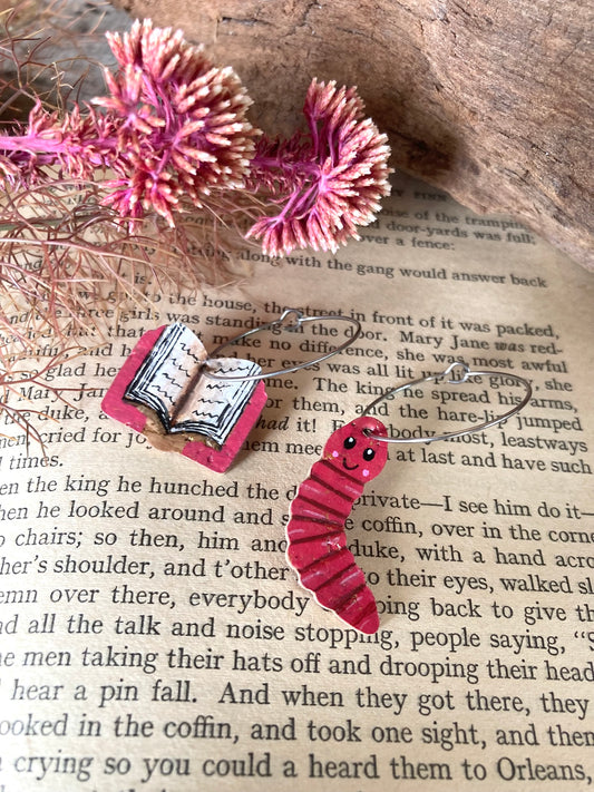 Handpainted mismatched cork bookworm earrings on silver hoops — pink open book and pink worm charms on open vintage book pages with pink dried flowers and cork bark