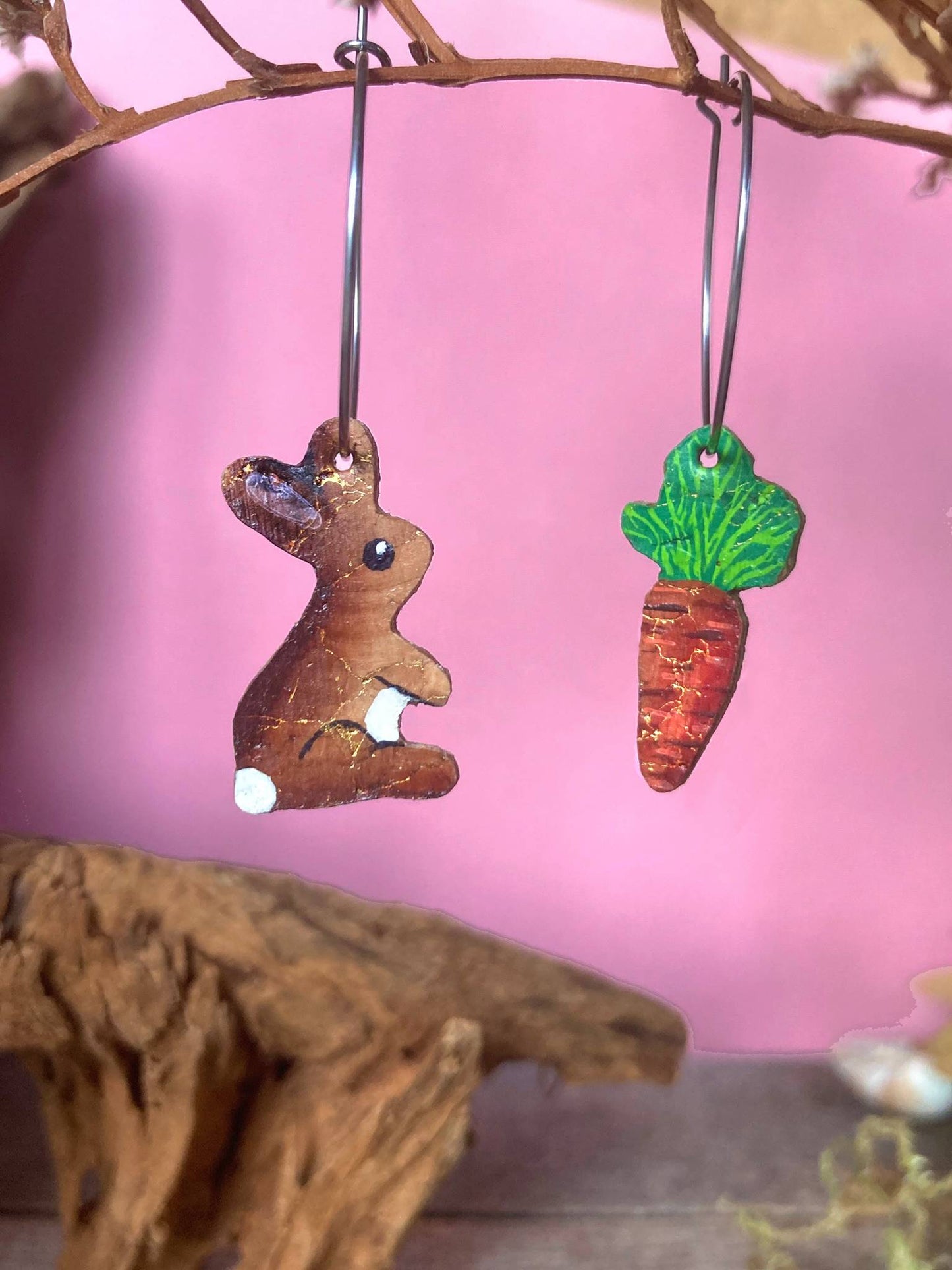 Cork rabbit and carrot hoop earrings hanging against a soft pink background.