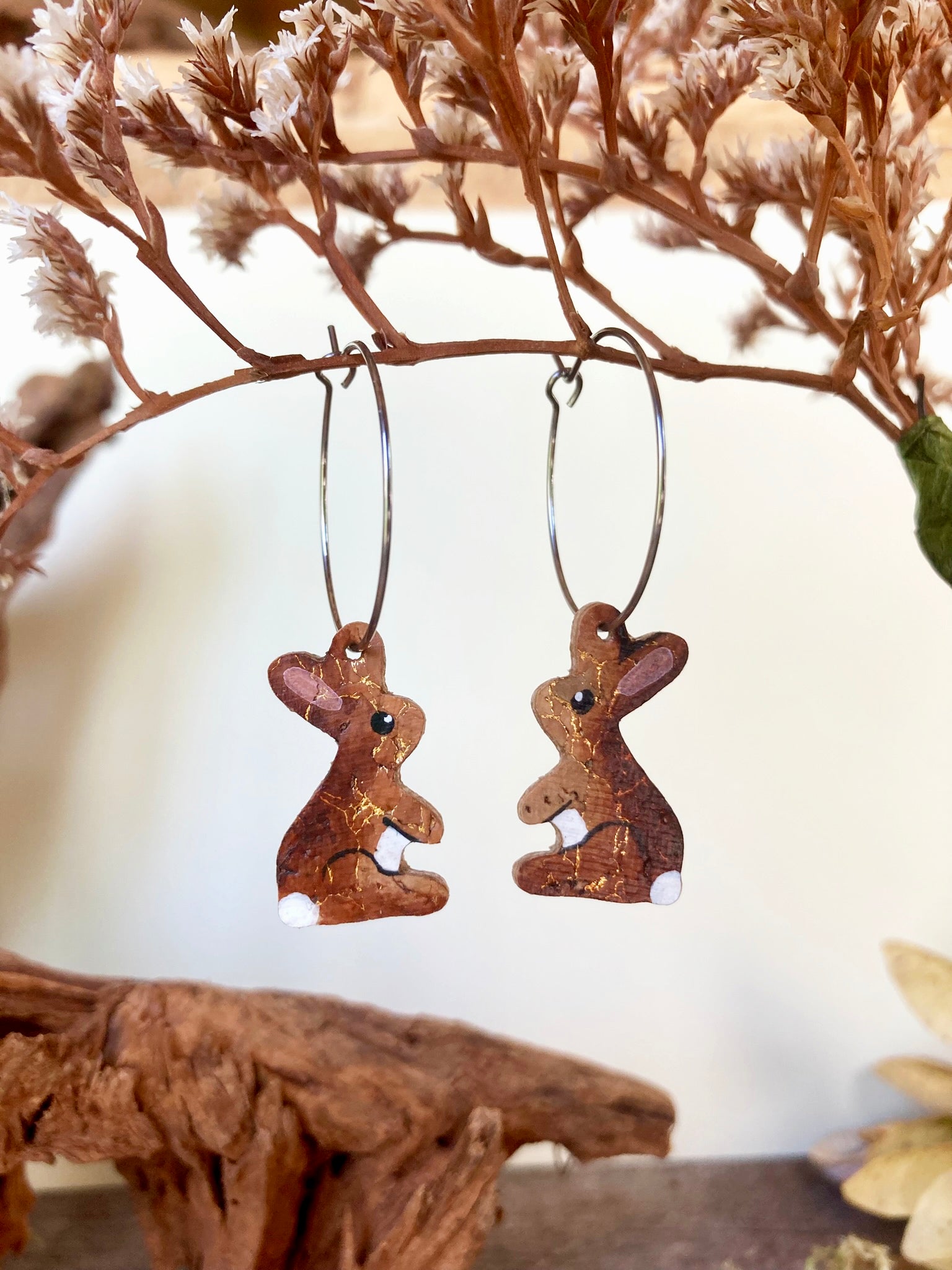 Cork rabbit hoop earrings hanging from a dried botanical branch against a soft cream background