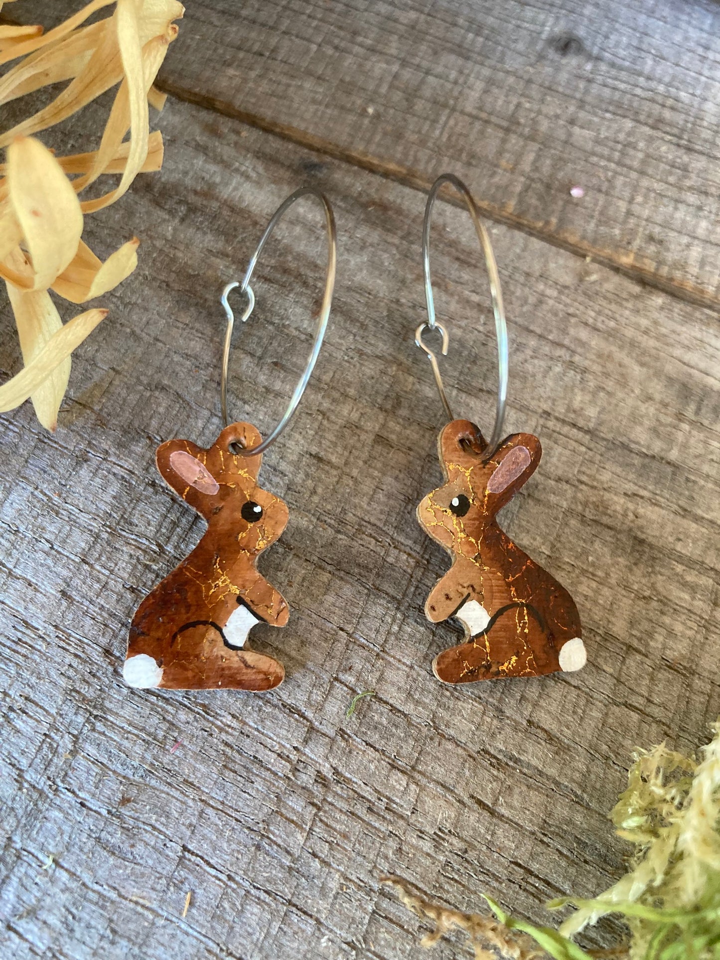 Pair of cork rabbit hoop earrings with gold fleck detail, laid on a weathered wooden surface with yellow dried flowers.