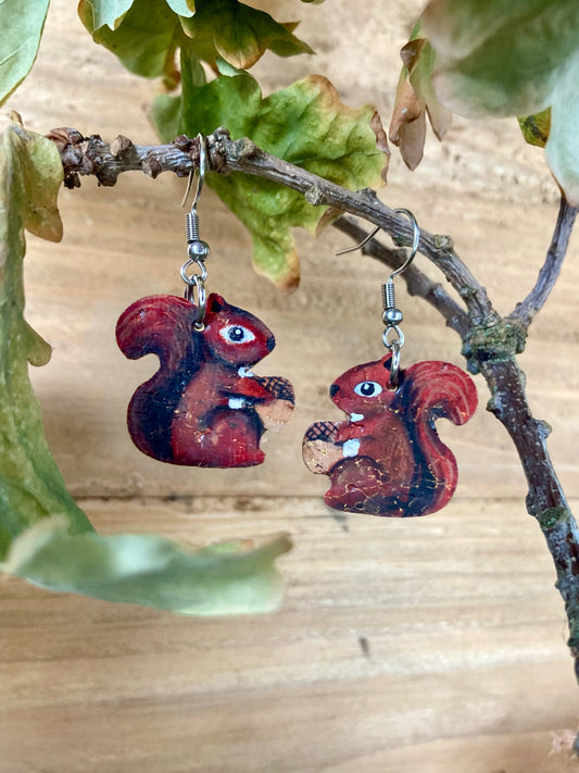 Handpainted cork red squirrel earrings hanging from a woodland branch with green leaves — russet tones with gold fleck