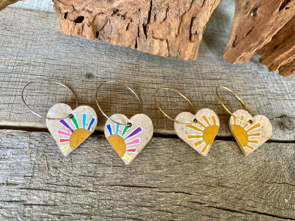 Rainbow multicoloured and yellow sun heart cork earrings on hoops, flat lay on weathered wood showing both colourways