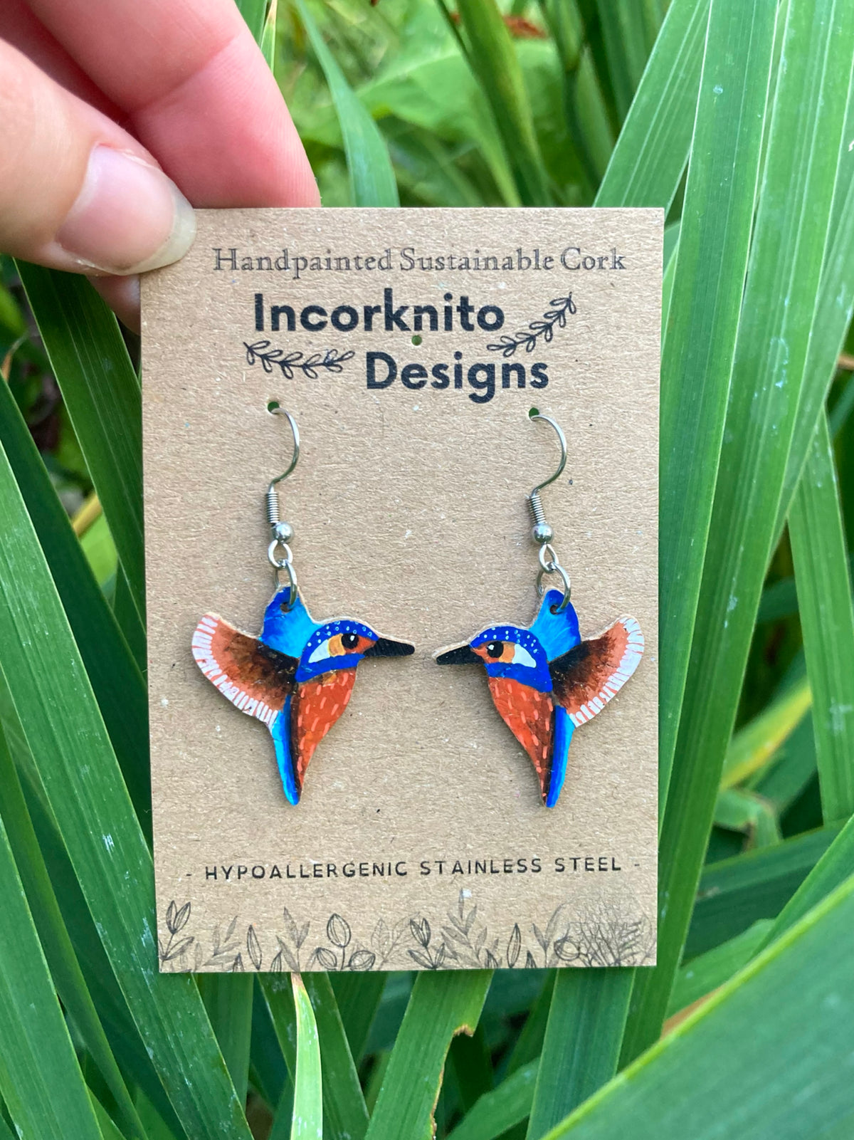 Kingfisher cork earrings on silver hooks on Incorknito Designs card against green reeds — handpainted British wildlife jewellery