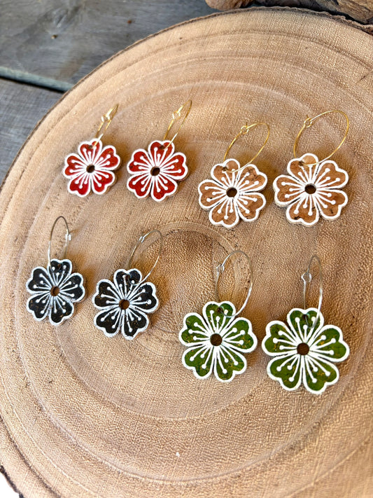 Large flower cork hoop earrings in all four colourways — natural, rust, green and black — on a wood slice, handmade in Suffolk UK