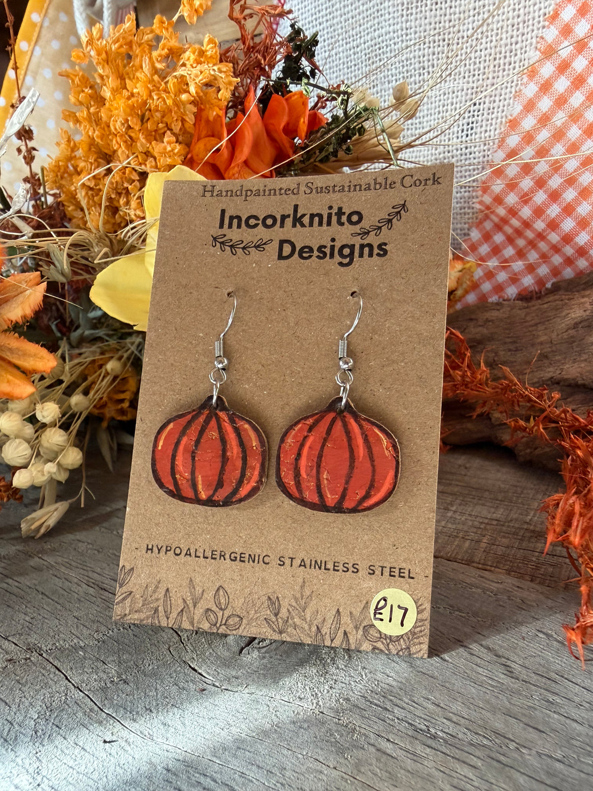 Handpainted large pumpkin cork earrings with silver hooks on an Incorknito Designs card, surrounded by dried flowers and autumn foliage