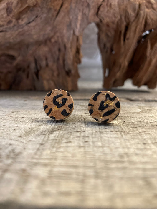 Handpainted leopard print cork stud earrings with black spots on warm natural cork on a driftwood surface