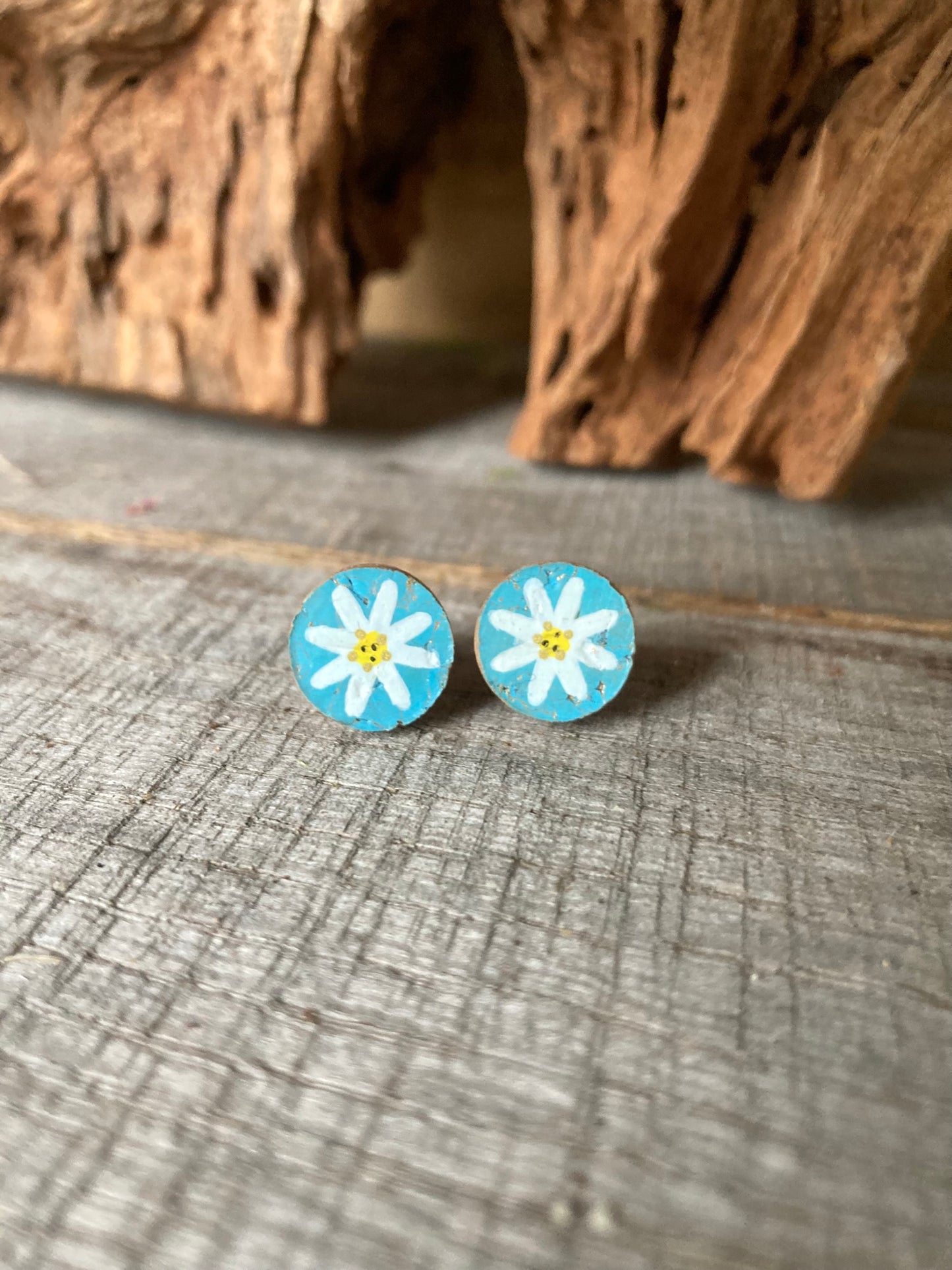 Light blue daisy cork stud earrings with white petals and yellow centre on a wooden surface
