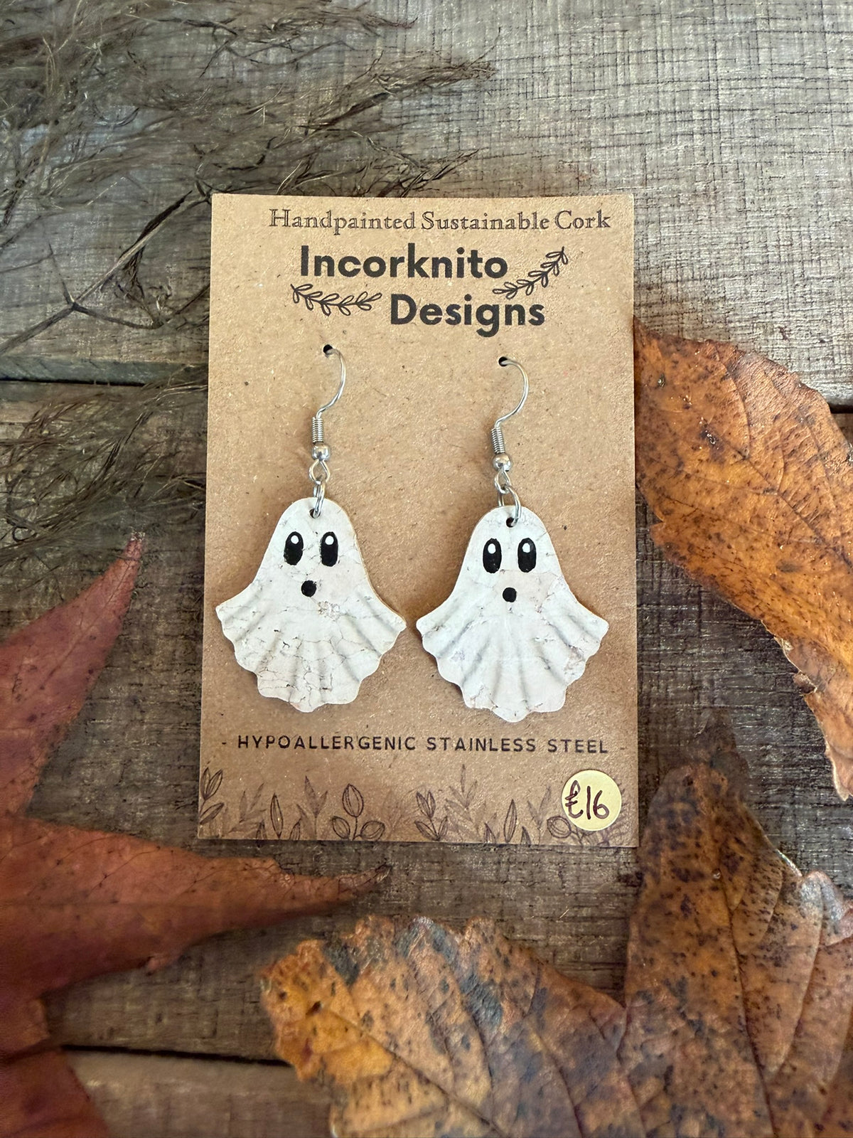 White cork ghost drops with black oval eyes and little open mouths, displayed on hooks among autumn leaves.