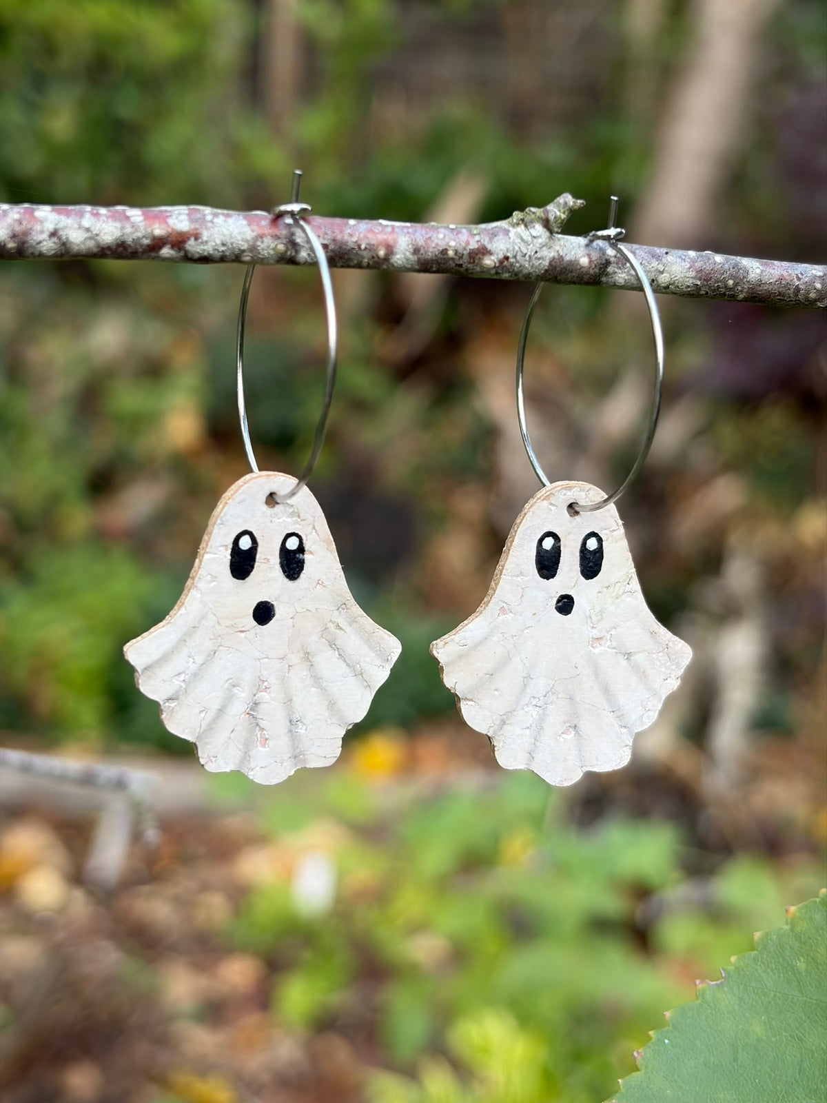 Angled view of cork ghost earrings on hoops, showing their flared shapes, scalloped edges and painted folds.