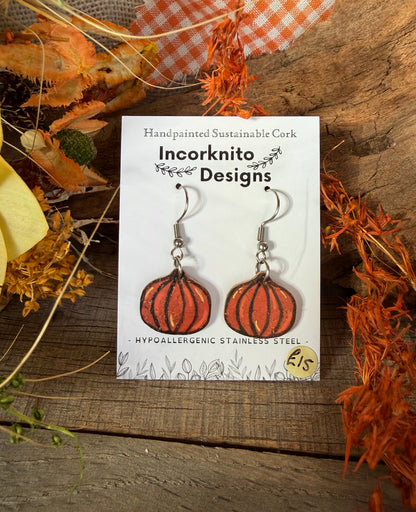 Mini pumpkin cork earrings with silver hooks on an Incorknito Designs card, surrounded by autumn foliage and orange gingham fabric