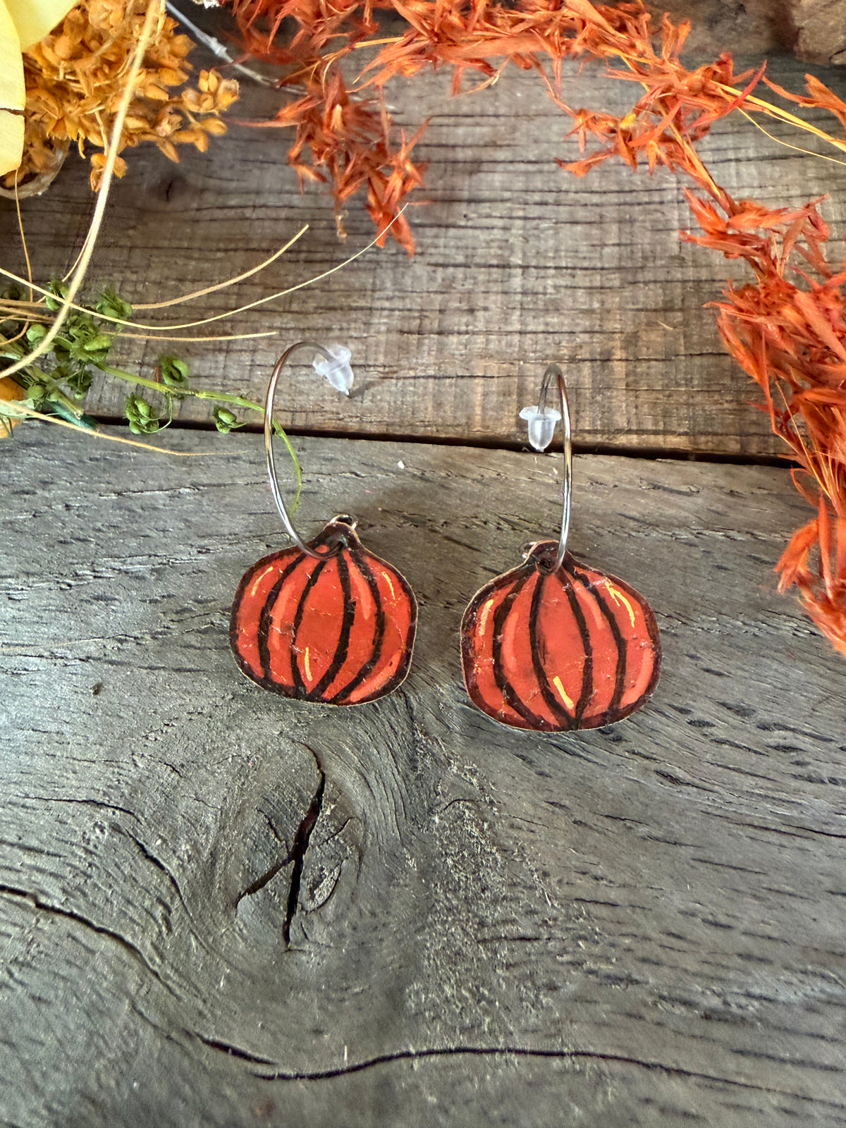 Lightweight orange pumpkin cork earrings with silver open back hoops and clear rubber backs, styled on rustic wood beneath autumn foliage.