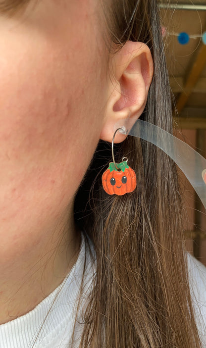 Close-up of a Mini Smiley Pumpkin cork earring worn on a silver open back hoop, showing how the charm hangs below the earlobe.