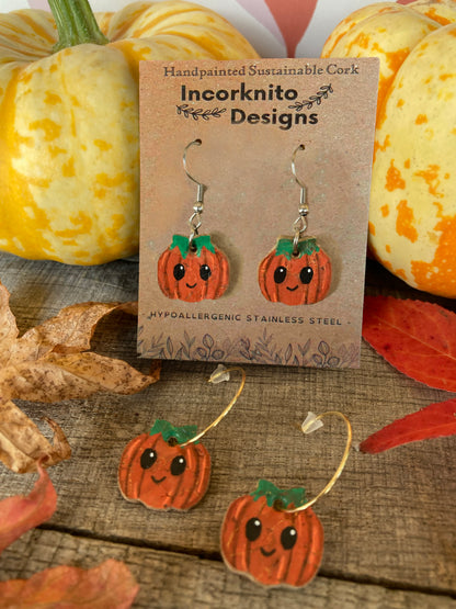  Mini Smiley Pumpkin earrings shown with silver hooks on a kraft display card and gold open back hoops below, surrounded by pumpkins and fallen leaves.