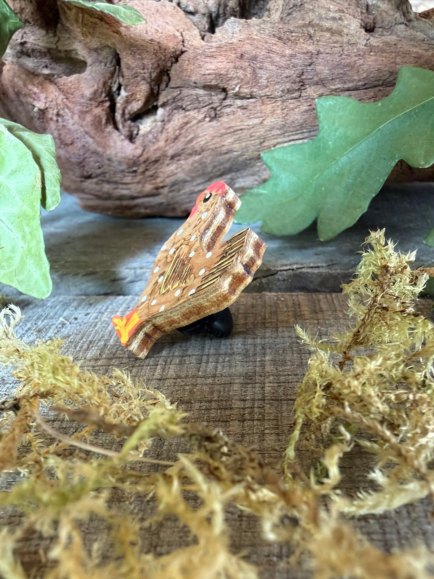 Side profile of the natural chicken cork pin badge on weathered wood with dried moss and oak leaves — showing cork layers and FSC ply base