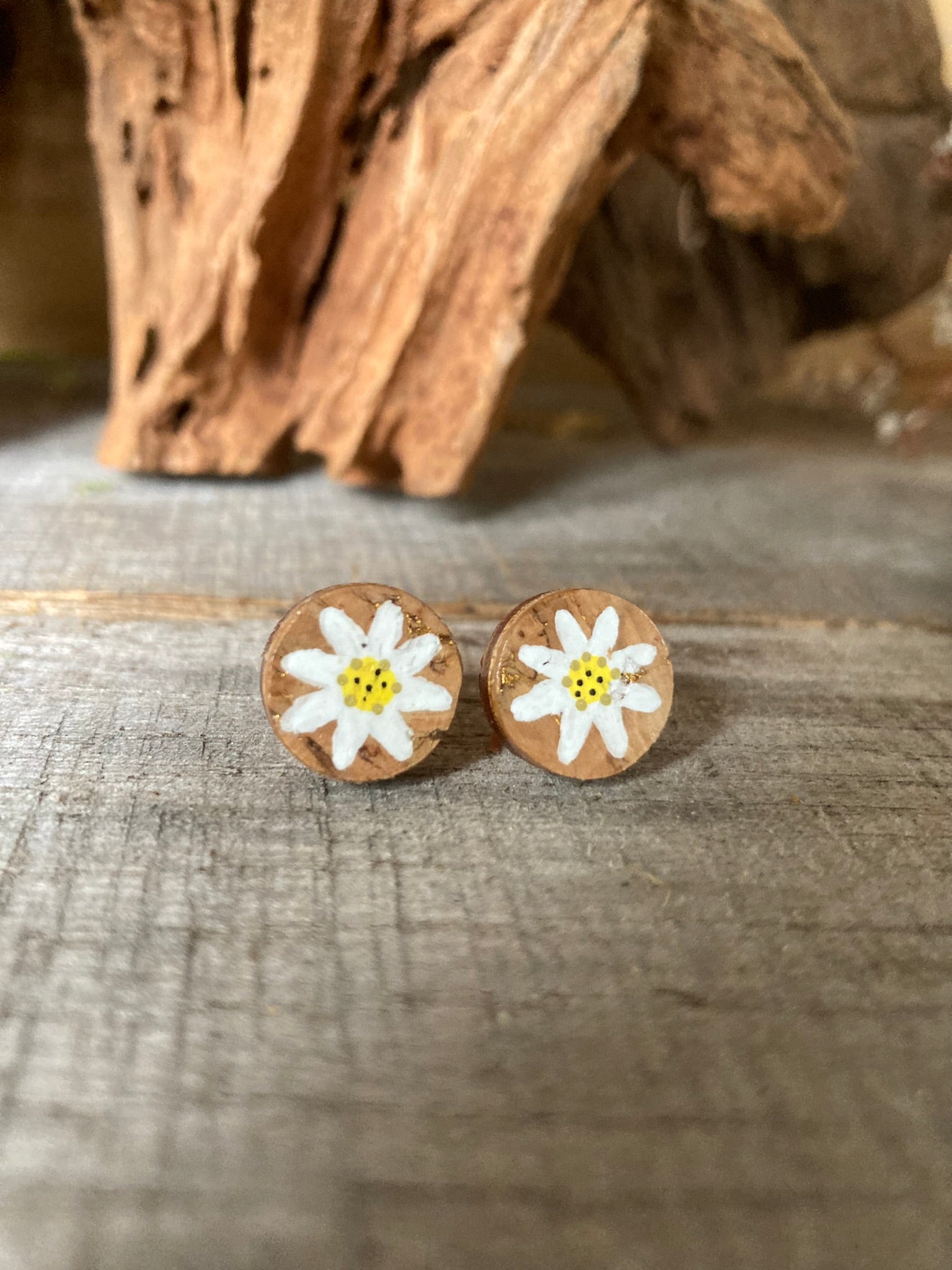 Natural cork daisy stud earrings with white daisy on uncoloured cork background on a wooden surface