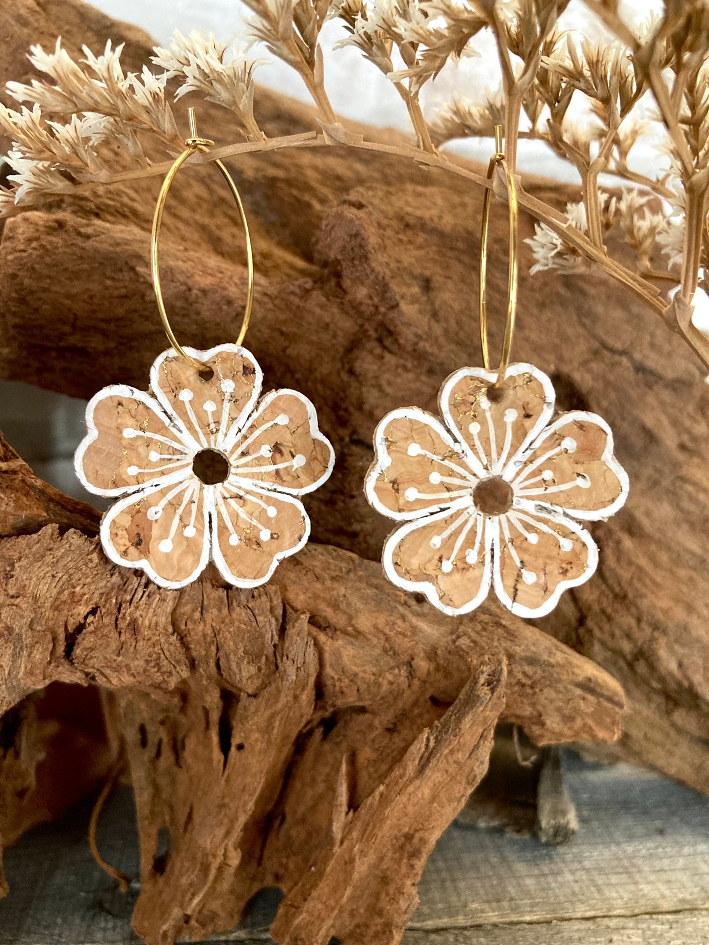 Natural large flower cork hoop earrings hanging from driftwood with dried botanicals — gold hoops with handpainted white pollen detail, handmade in Suffolk UK