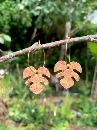 Natural cork monstera earrings on gold hoops catching sunlight on a garden branch — gold fleck detailing glinting in natural light