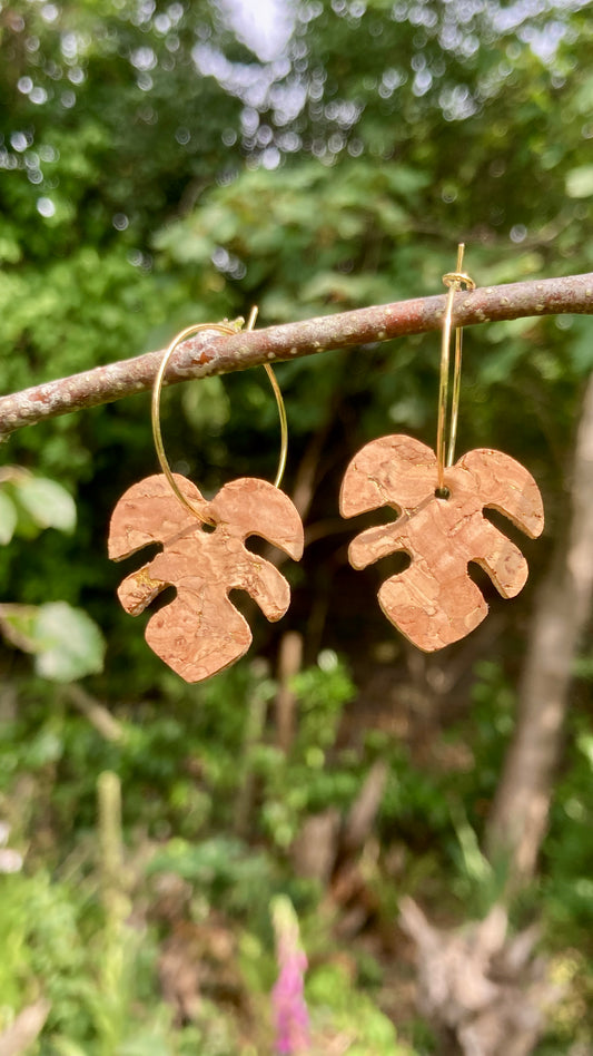 Natural cork monstera earrings on gold hoops hanging from a garden branch — handmade sustainable plant jewellery by Incorknito Designs