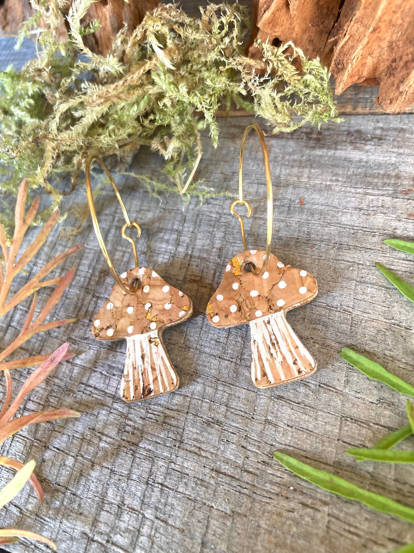 Natural toadstool cork large hoop earrings flat lay on weathered wood with botanicals — gold hoops showing the natural cork texture and white spot detail