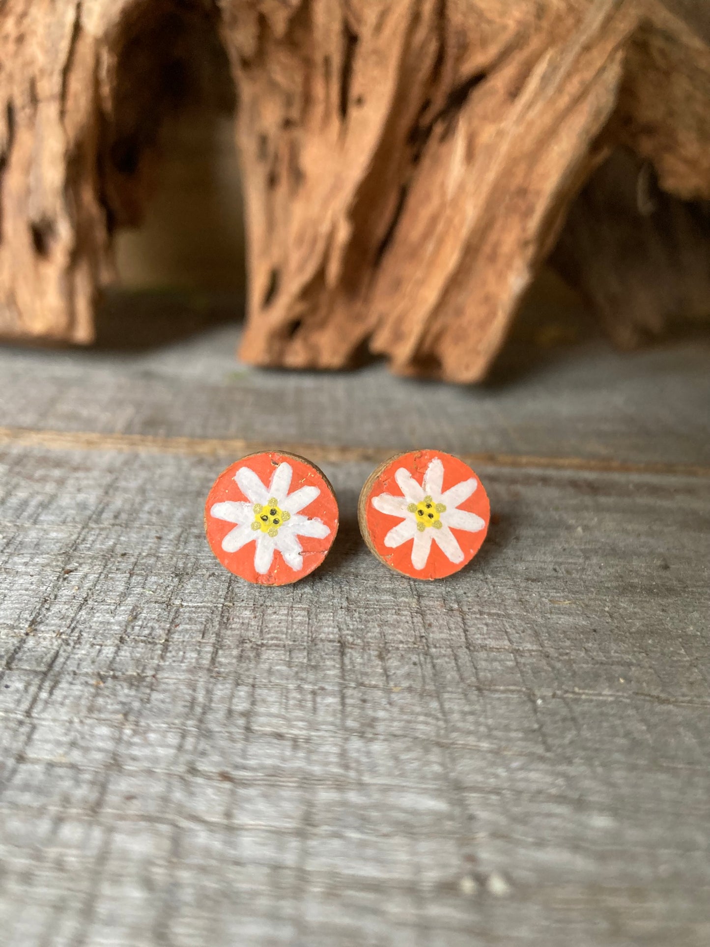 Orange daisy cork stud earrings with white petals and yellow centre on a wooden surface