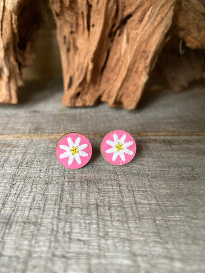 Pink daisy cork stud earrings with white petals and yellow centre on a wooden surface