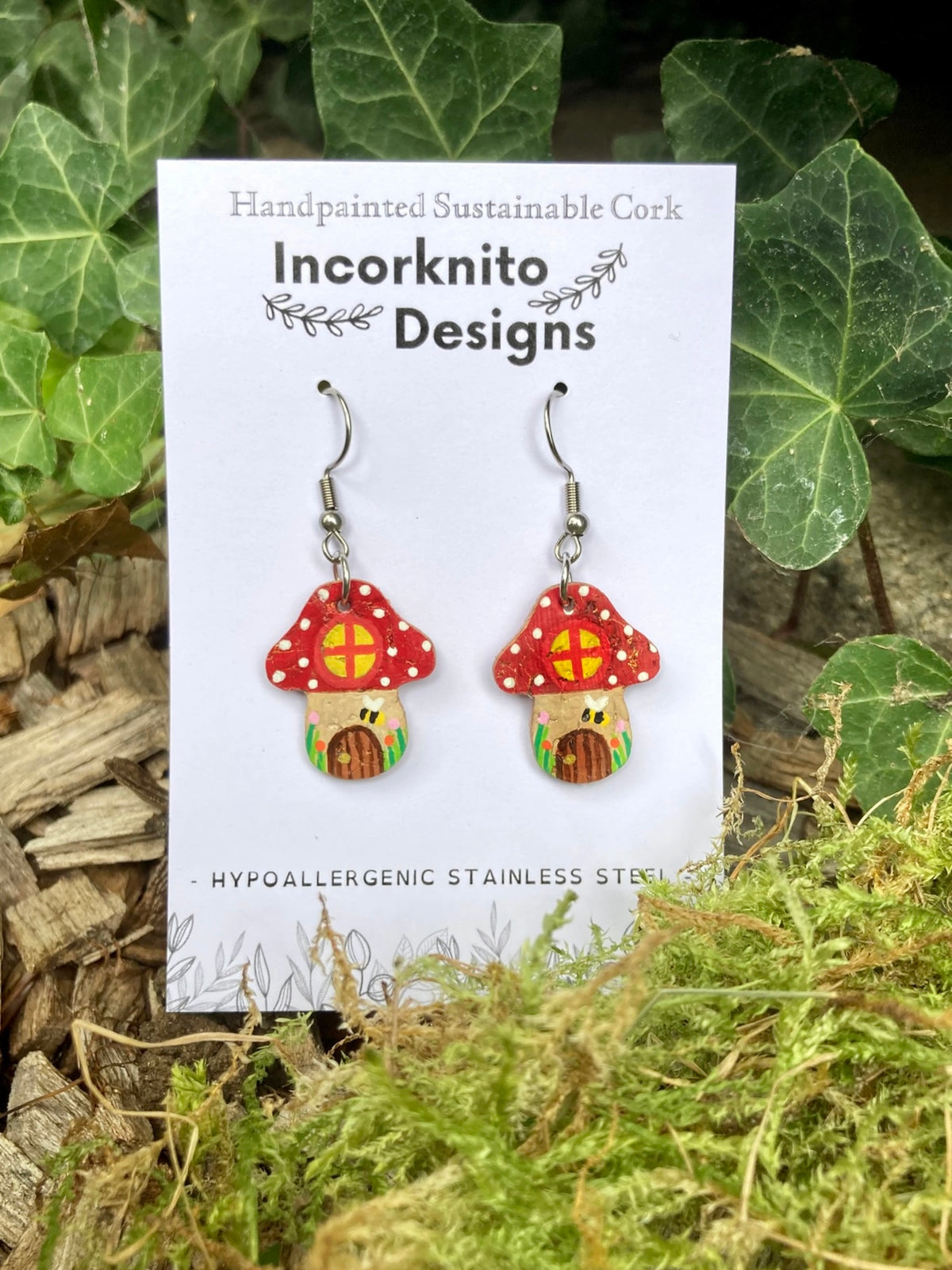 Red Fairy House Toadstool Earrings on hooks — handpainted cork showing window, door and bee detail, on Incorknito Designs card with ivy background