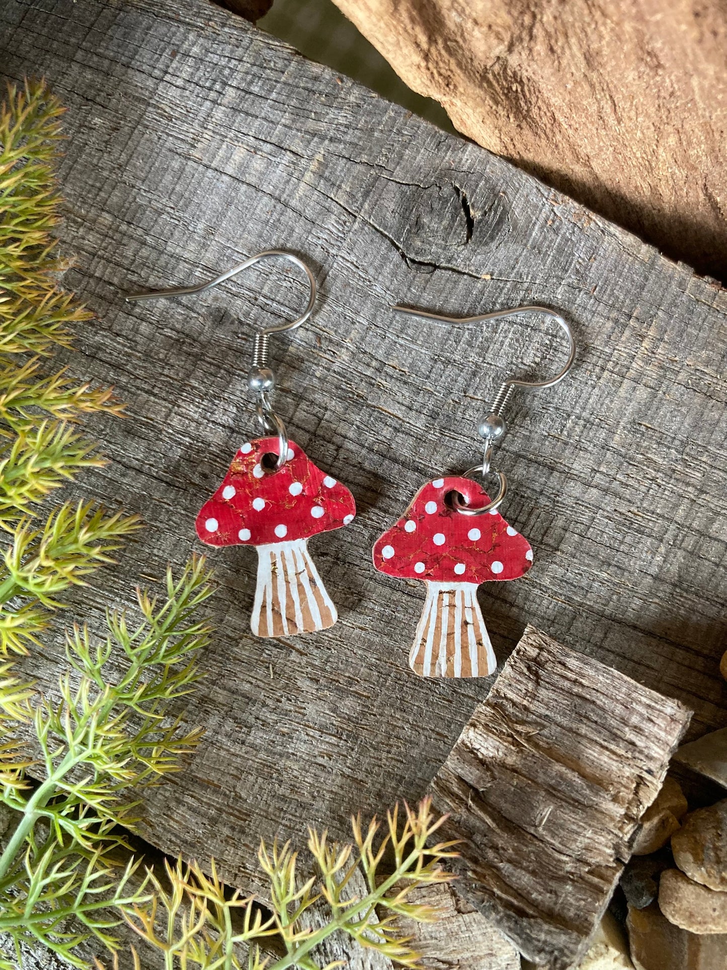 Red toadstool cork medium earrings flat lay on weathered wood with moss — handpainted fly agaric design with white spot detail, handmade in Suffolk UK