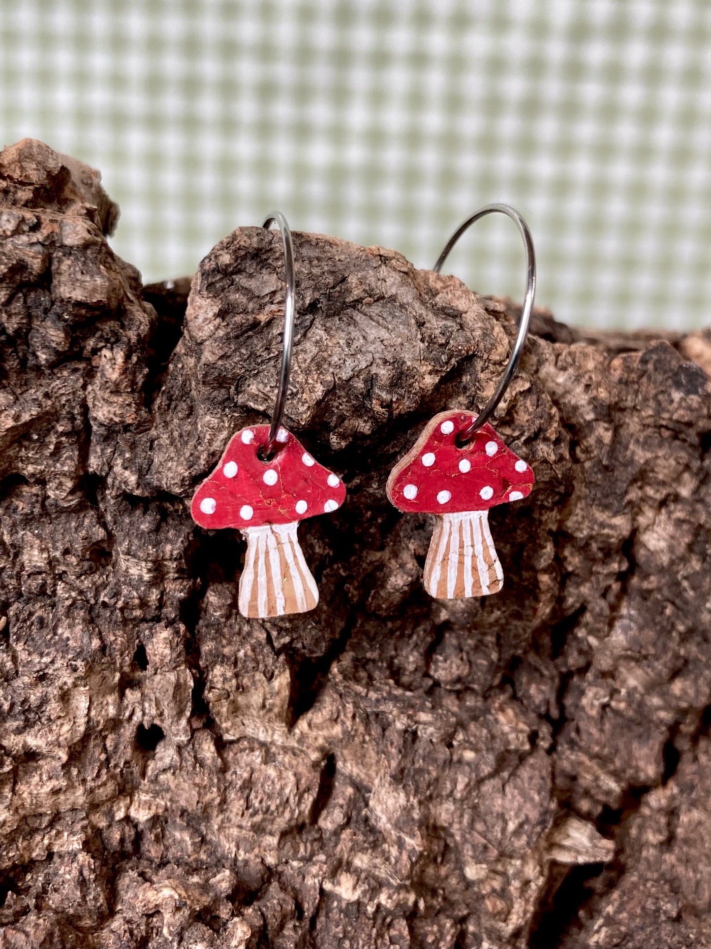 Red toadstool cork mini hoop earrings resting on cork bark — showing the natural cork texture and handpainted fly agaric detail up close