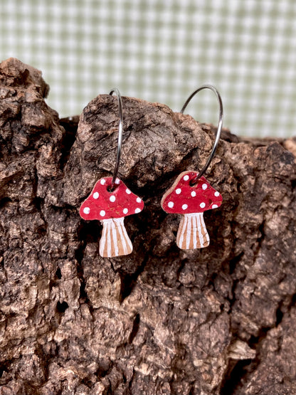 Red toadstool cork mini hoop earrings resting on cork bark — showing the natural cork texture and handpainted fly agaric detail up close