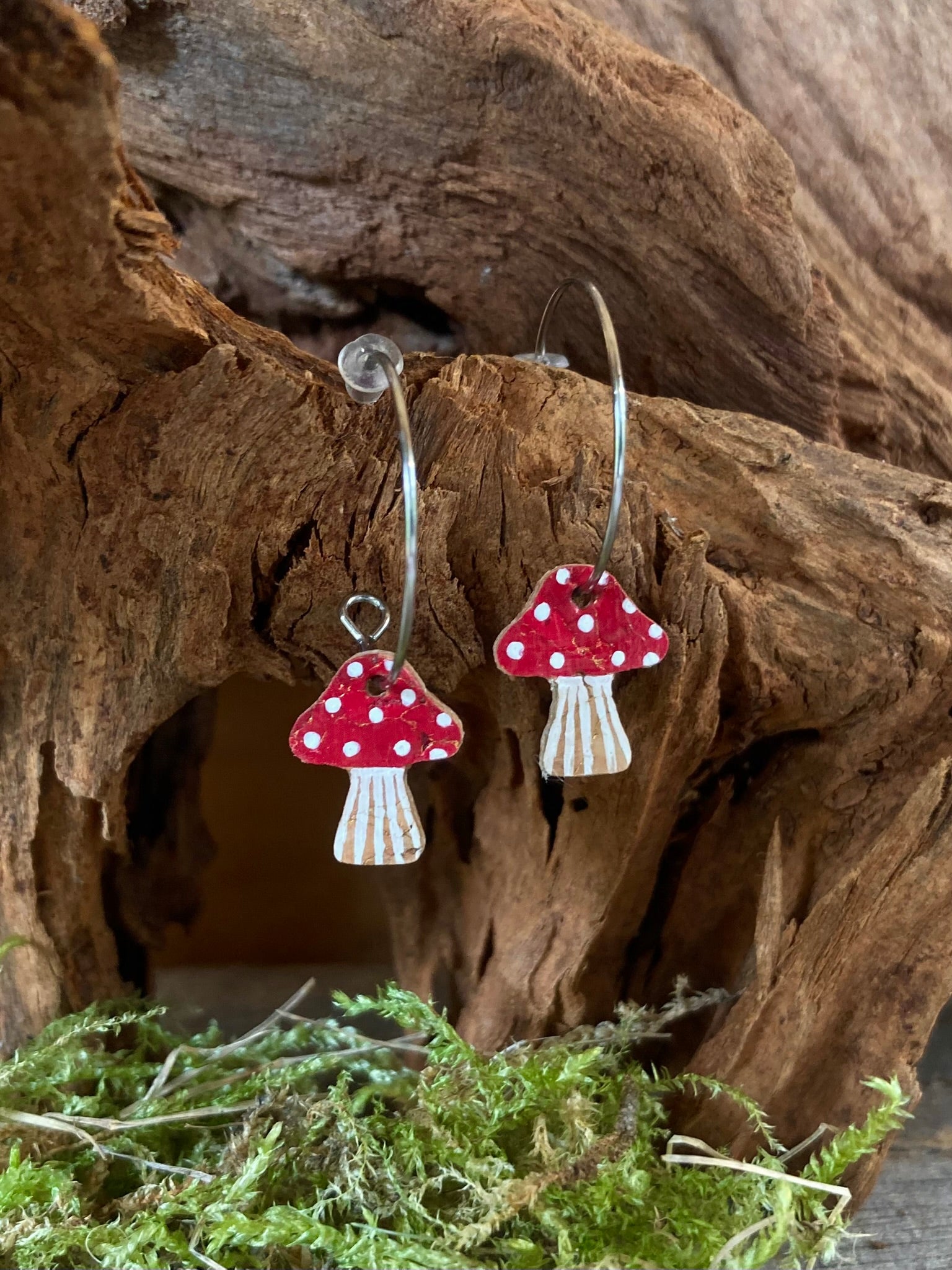 Red handpainted toadstool cork mini hoop earrings nestled in a driftwood hollow with moss — fly agaric design, handmade in Suffolk UK