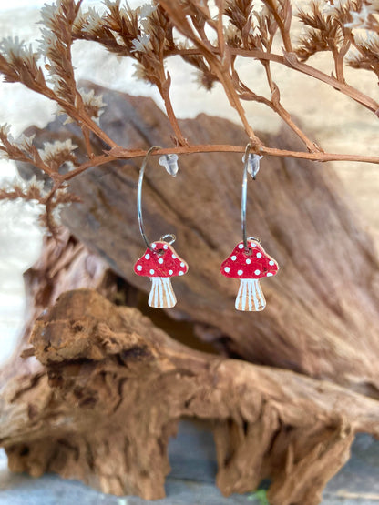 Red toadstool cork mini hoop earrings hanging from dried russet botanicals — handpainted fly agaric design with white spots on a rich red cap