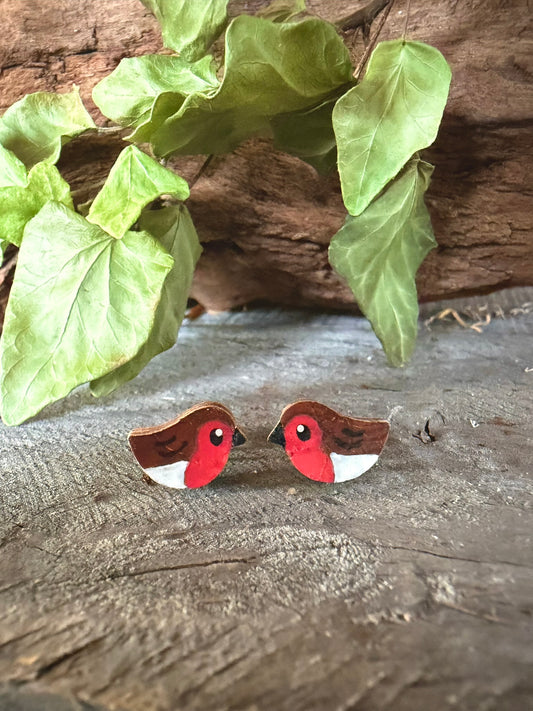Handpainted robin cork stud earrings with vivid red breast and brown wings on a driftwood surface with ivy