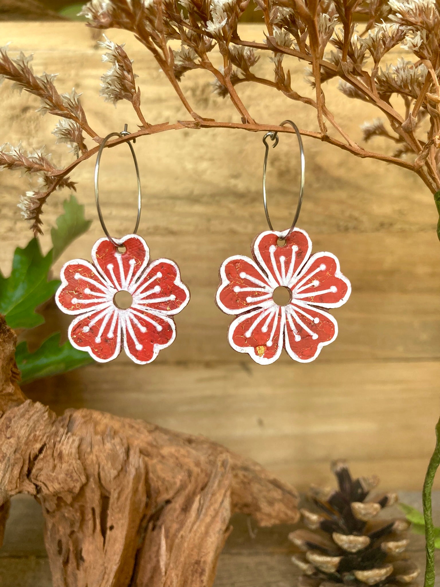 Rust large flower cork hoop earrings hanging from dried botanicals — silver hoops with warm rust handpainted design and white pollen detail
