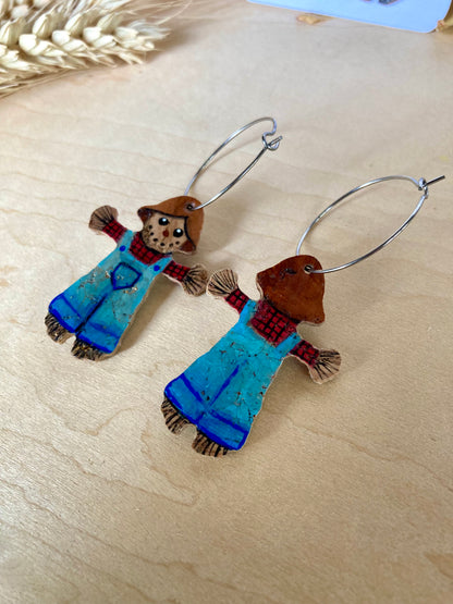 Front and reverse view of handpainted cork scarecrow earrings — face detail on front, back of hat visible on reverse