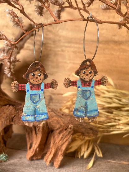 Gold-flecked cork scarecrow earrings catching the light on silver hoops, styled with dried botanicals