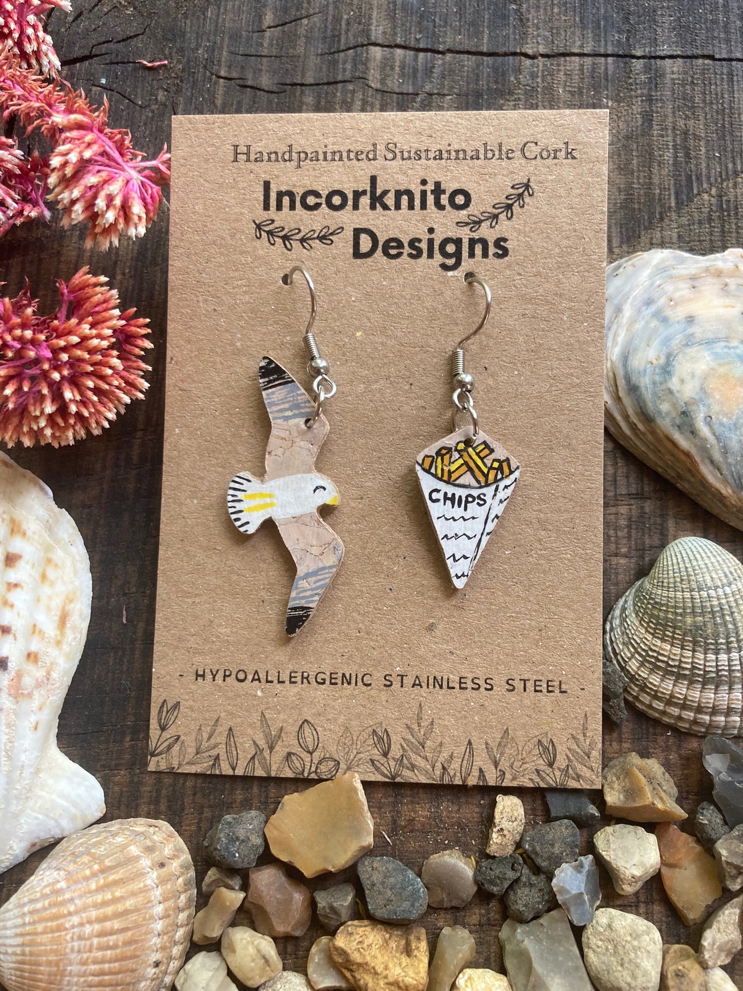 Handpainted seagull and chips mismatched cork earrings on silver hooks on Incorknito Designs card surrounded by seashells and stones — quirky coastal jewellery handmade in Suffolk UK