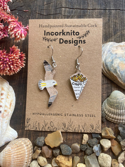 Handpainted seagull and chips mismatched cork earrings on silver hooks on Incorknito Designs card surrounded by seashells and stones — quirky coastal jewellery handmade in Suffolk UK