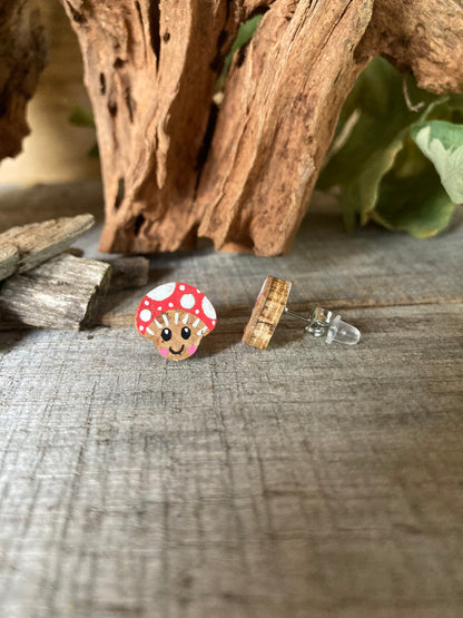 Smiley toadstool cork stud earrings on a driftwood surface with wild greenery. Side view of FSC wood with backing options