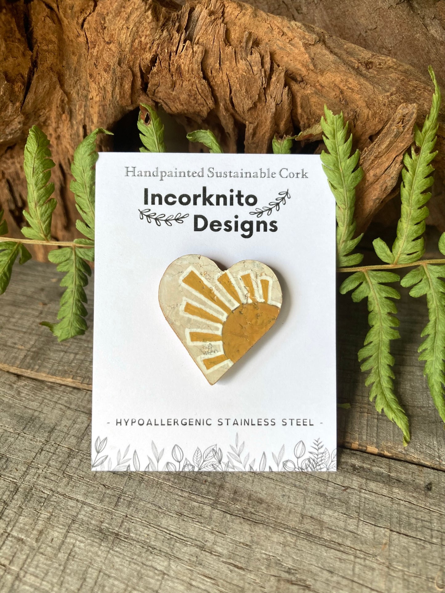 Sun cork pin badge on Incorknito Designs branded card against driftwood and green ferns — handpainted sustainable badge handmade in Suffolk UK