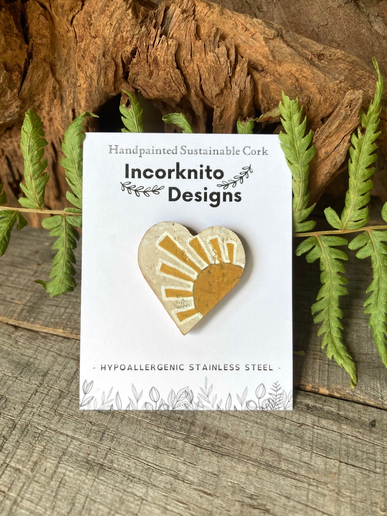 Sun cork pin badge on Incorknito Designs branded card against driftwood and green ferns — handpainted sustainable badge handmade in Suffolk UK