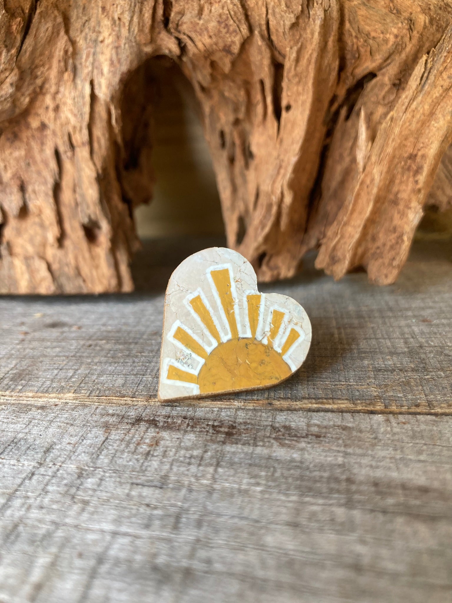 Heart-shaped sun cork pin badge flat lay on weathered wood — handpainted golden rising sun design, eco-friendly badge handmade in UK