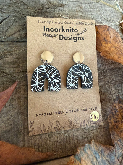 SW1 arch-shaped spider-web cork earrings with silver disc stud tops, featuring fine white webs on black cork, displayed on a kraft card.