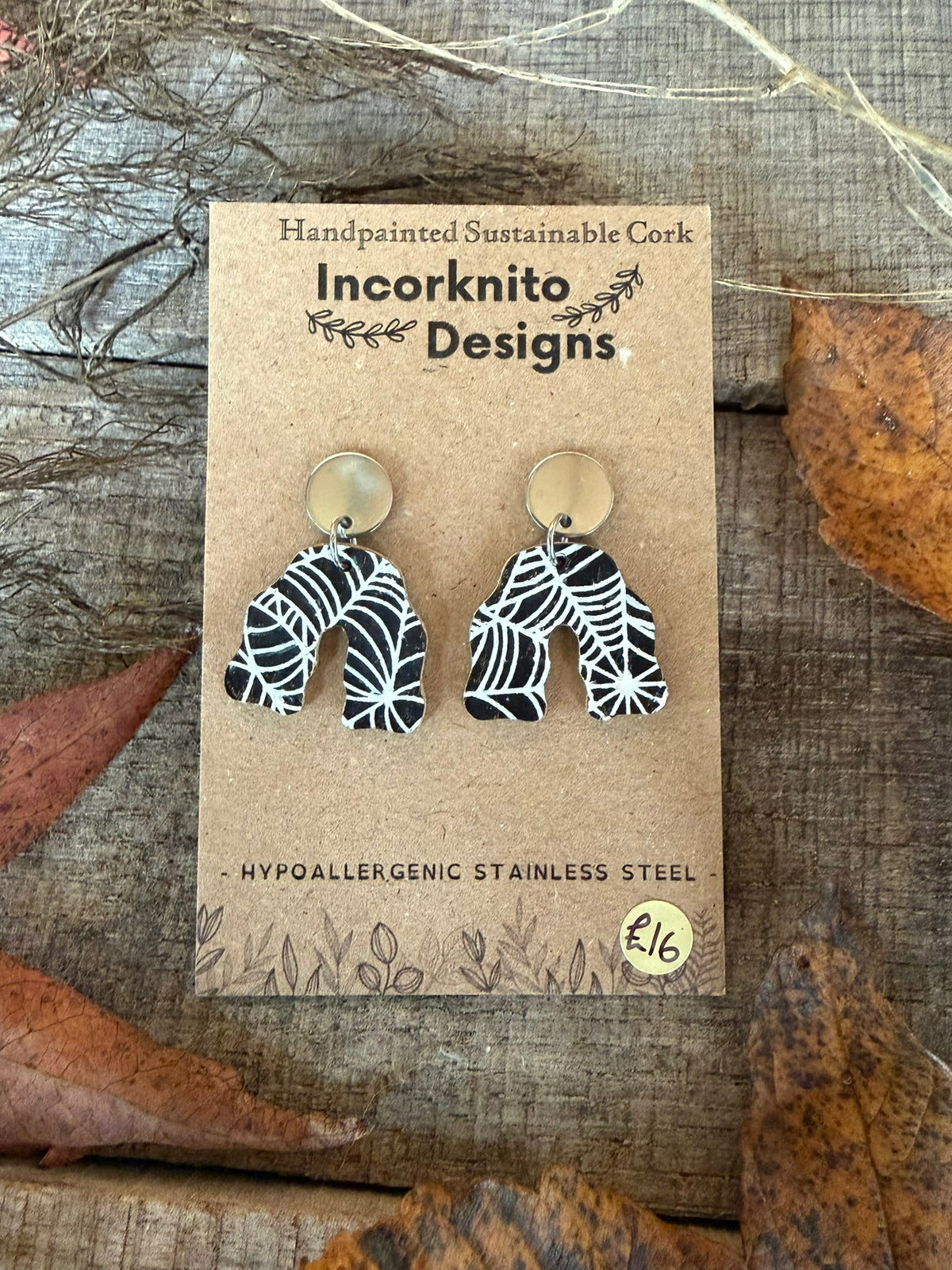 SW3 wavy arch cork earrings with silver disc stud tops, decorated with contrasting white spider webs on a black background.
