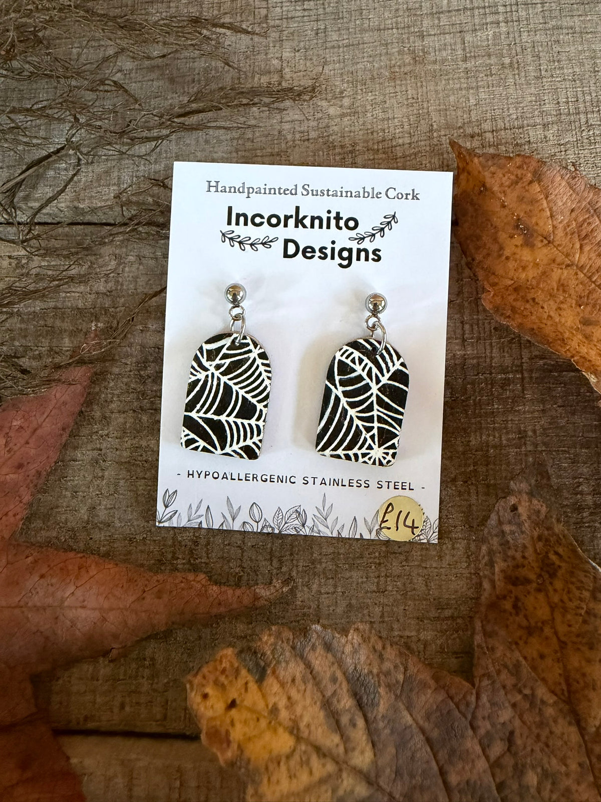 SW4 rounded rectangle spider-web earrings hanging from silver ball studs, with white web patterns painted across black cork on a white display card.
