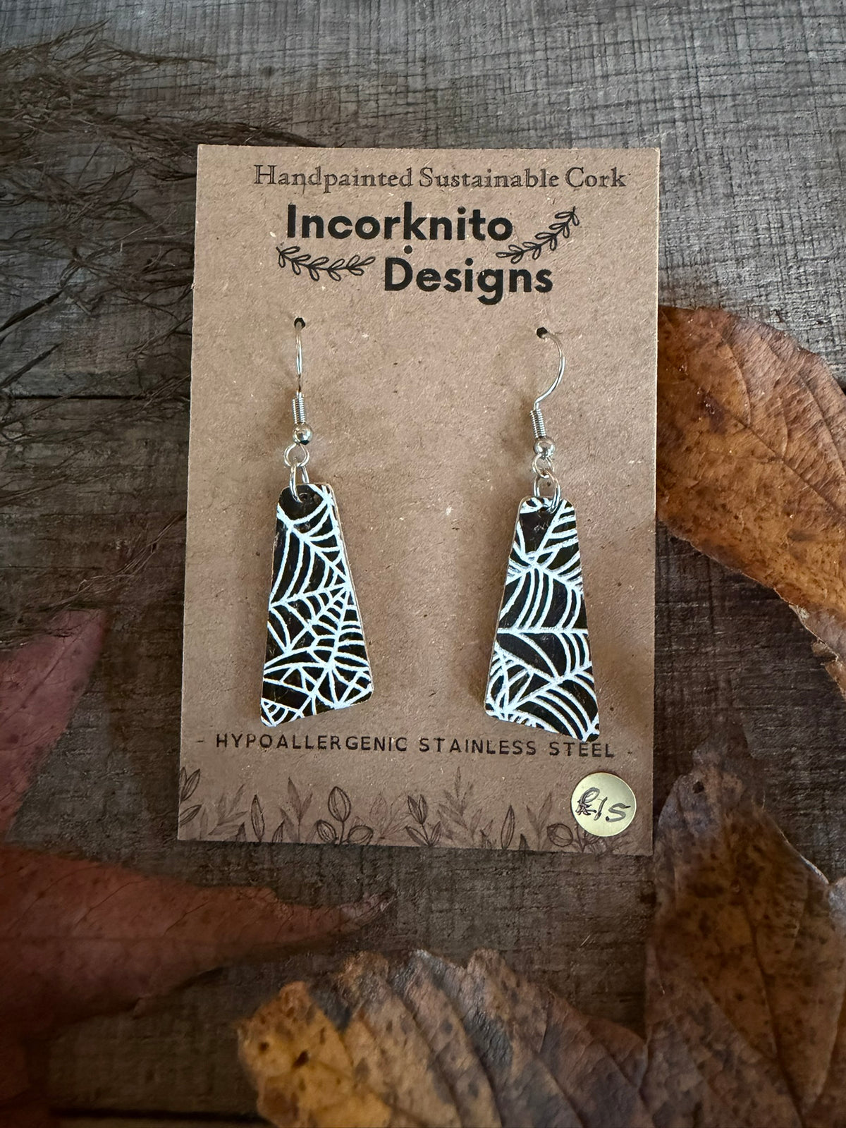 SW6 wide tapered spider-web cork earrings on silver hooks, with an intricate arrangement of white webs across the black painted surface.