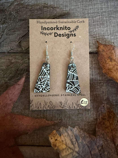 SW7 tapered black cork earrings with silver hooks, featuring a white web centre near the lower left of the pictured pair, styled beside fallen leaves.