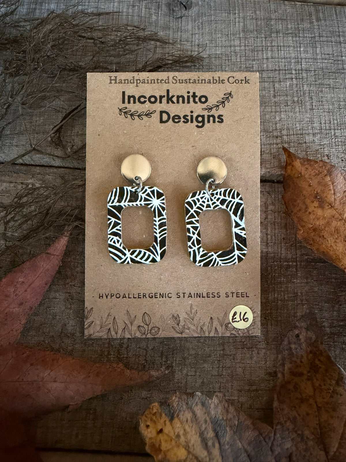 SW8 open rectangle cork earrings with silver disc stud tops, featuring white spider-web patterns around rectangular cut-outs on a black background.