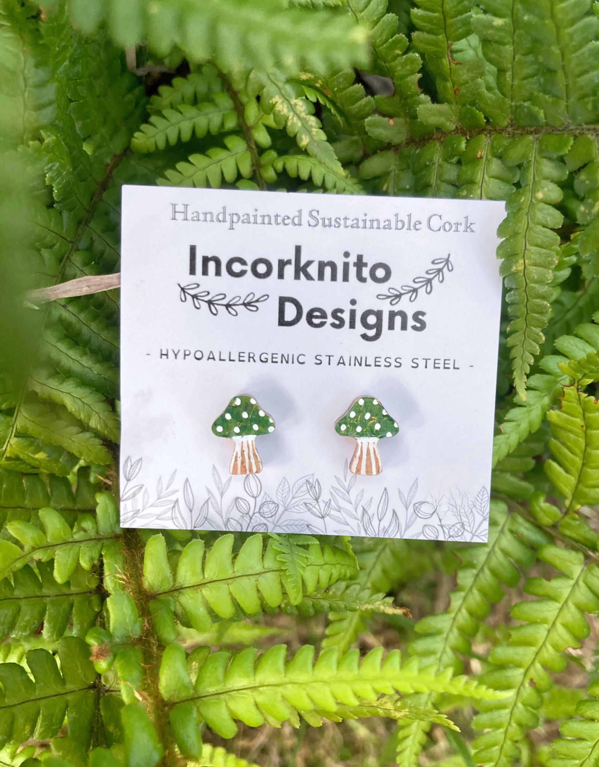 Incorknito Designs branded card with toadstool cork stud earrings on a green leaf background